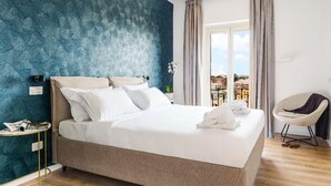 A neatly made bed with white linens, a small bedside table with a lamp, and a chair with a cushion. - Elysium Suites Colosseo (Rome)