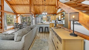 Un vaste espace de vie doté d’un plafond en bois, d’un canapé gris, d’une cuisine avec des meubles en bois et d’un escalier.