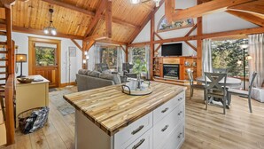 Un vaste espace de vie doté d’un plafond en bois, d’une cheminée, d’un téléviseur et d’une table à manger avec des chaises.