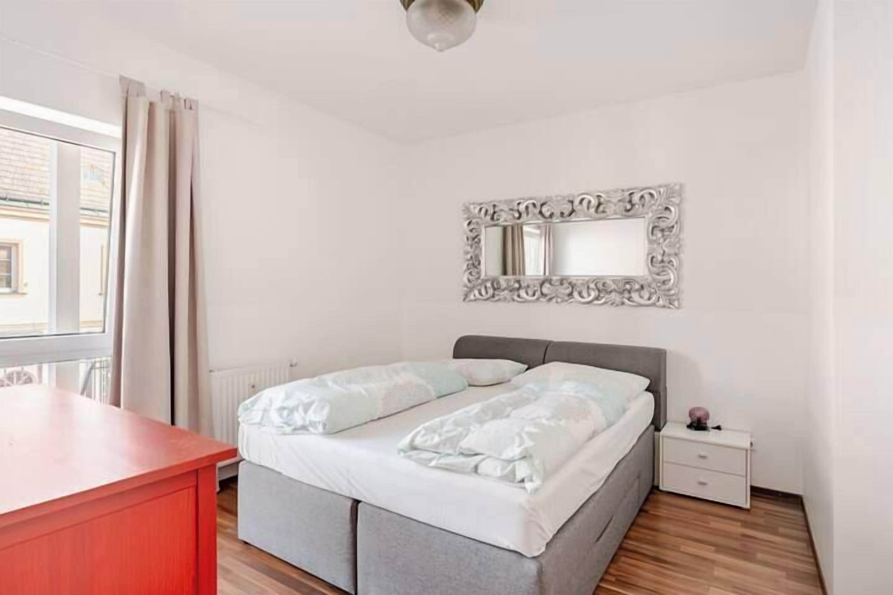 A bedroom with a bed, a nightstand, a dresser, and a mirror on the wall.