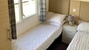 Una habitación pequeña con una cama individual, cabecera de madera, lámpara de noche y ventana con cortinas.