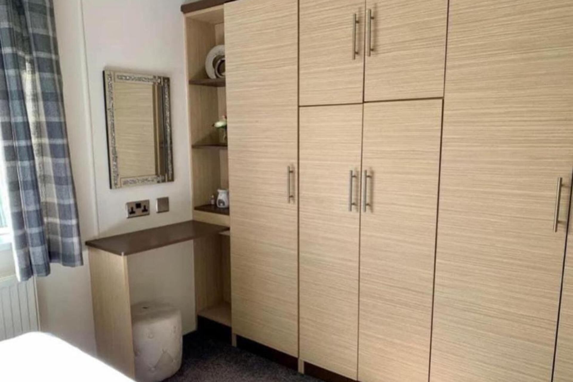 Quarto com armário de madeira, prateleira pequena com espelho e vaso sanitário branco.