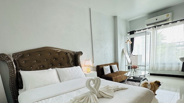 A hotel room with a large bed, a small table with a lamp, a mirror, and a window with curtains. - Service apartment lampang (Lampang)
