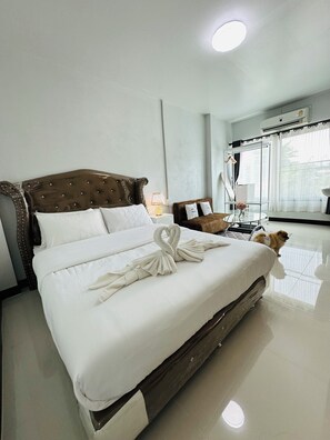 Habitación de hotel con una cama grande, una mesita con lámpara, un espejo y una ventana con cortinas.