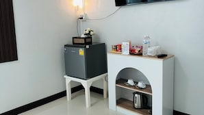 A modern hotel room with a flat-screen TV mounted on the wall, a small refrigerator, a coffee machine, and a shelf with snacks and a water bottle. - Service apartment lampang (Lampang)