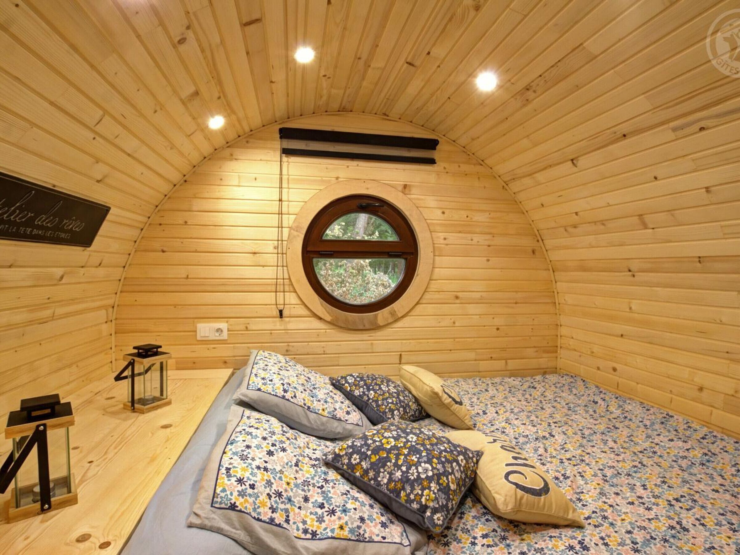 Un cuarto circular y acogedor de madera, con cama, almohadas y una ventana.
