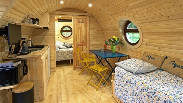 Uma cabana acolhedora com interior em madeira, sala de jantar, cama com roupa de cama floral e pequena cozinha.