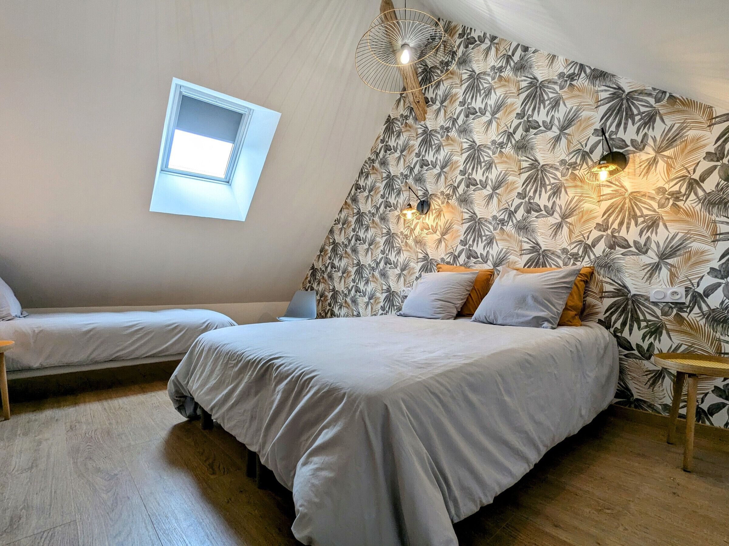 A bedroom with two beds, a window, and a wall with a leaf pattern.