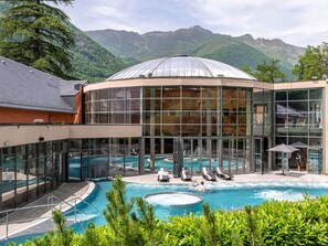 A hotel with a pool, glass walls, and a mountain backdrop.