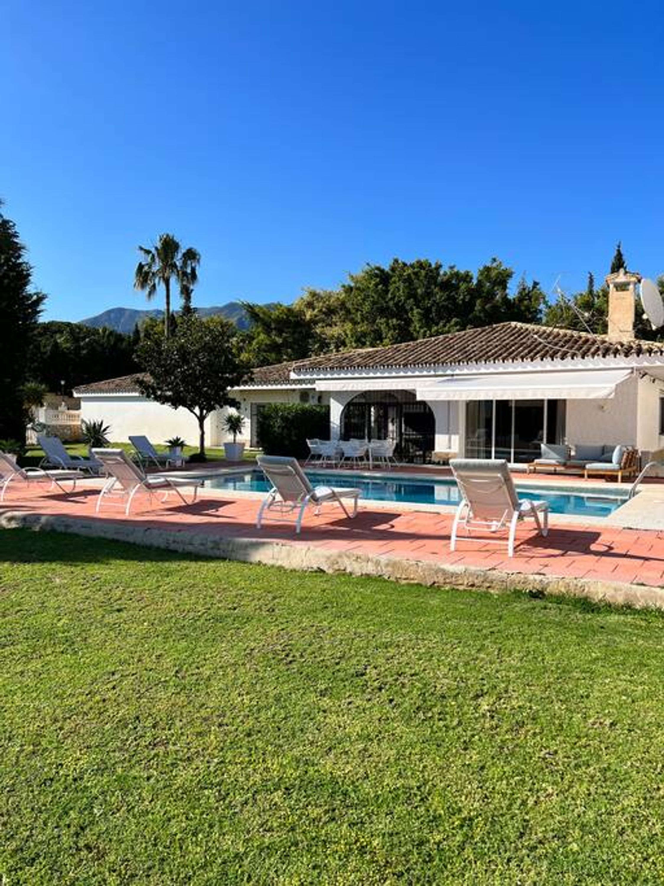 A poolside area with lounge chairs, a swimming pool, and a building with a tiled roof.