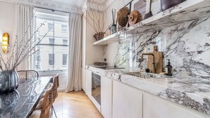Eine moderne Küche mit Marmorarbeitsplatten, einem Holzbruchbrett und Blick auf die Stadt durch große Fenster.