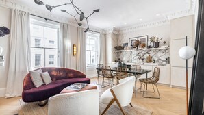 Ein modernes Wohnzimmer mit einem violetten Sofa, weißen Sesseln und einem Essbereich mit Korbstühlen.
