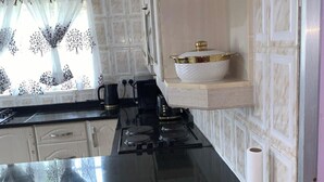 A kitchen with a black countertop, a stove, a coffee maker, and a decorative bowl on a shelf. - 4 Bed Gated House-sleeps 8-private Parking (Harare)
