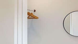 Um banheiro com porta branca, um suporte de madeira para cabides e um espelho redondo na parede.
