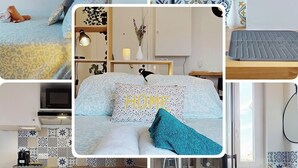 Quarto de hotel com cama, escrivaninha, pequeno espaço de cozinha, banheiro e área de chuveiro.