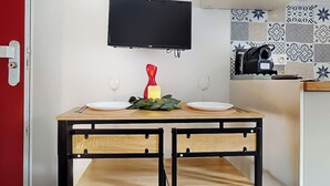 Cozinha compacta com mesa de madeira, duas cadeiras, uma TV de tela plana montada acima e um painel de fundo com padrão.