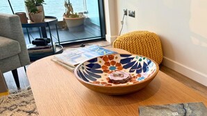 Una sala de estar moderna con una mesa redonda de madera, un cuenco decorativo y un pouf amarillo.
