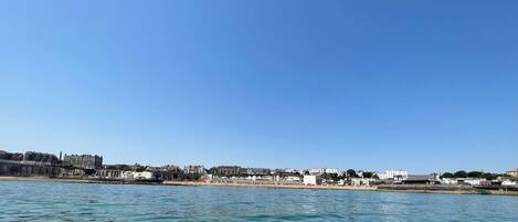 Paisatge urbà costaner amb edificis al passeig marítim, cel blau clar i mar tranquil·la.