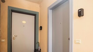 Ein Flur mit einer Tür, einem Mülleimer, einer Fußmatte und einem an der Wand befestigten Lichtschalter.