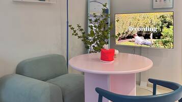 En moderne stue med et rundt bord, to stole, en sofa, en potteplante, et vægmonteret tv og en kalender.