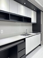 Una cocina moderna con armarios blancos, un lavamanos de acero inoxidable y una encimera negra.