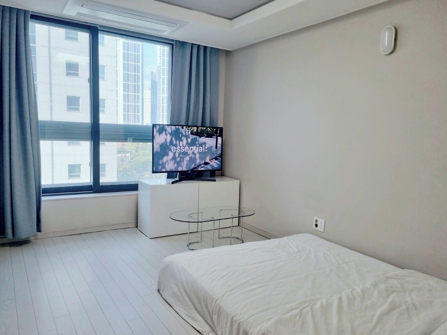 Ein modernes Hotelzimmer mit großem Fenster, Flachbildfernseher, Glastisch und Bett.
