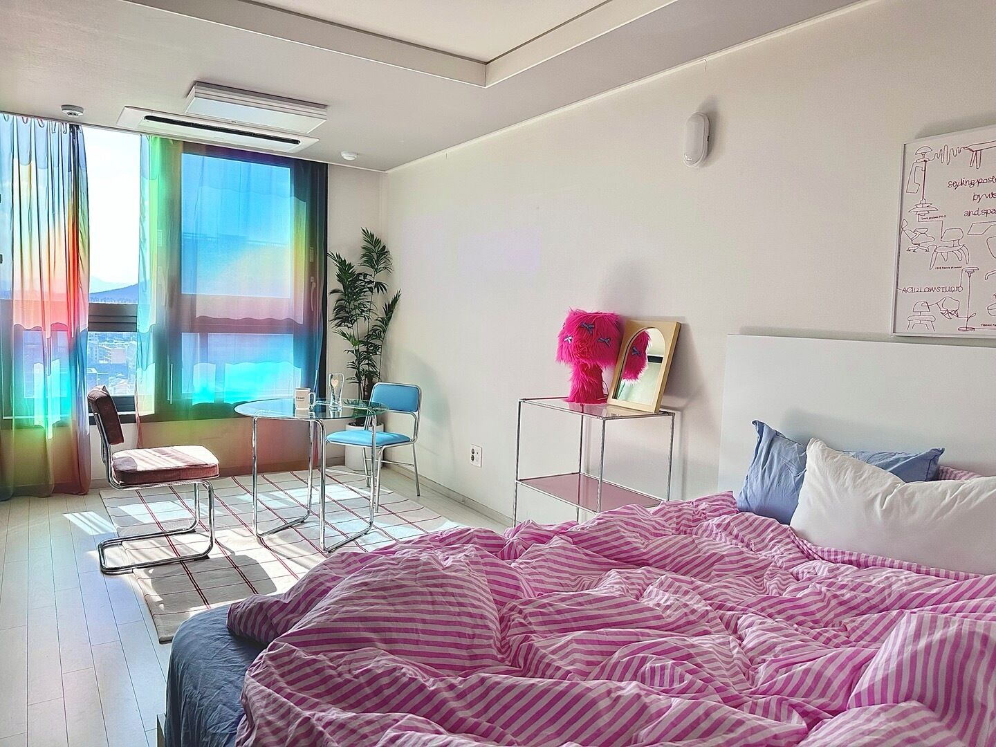 A bedroom with a bed, a small table with chairs, a window with curtains, and a wall with a poster.