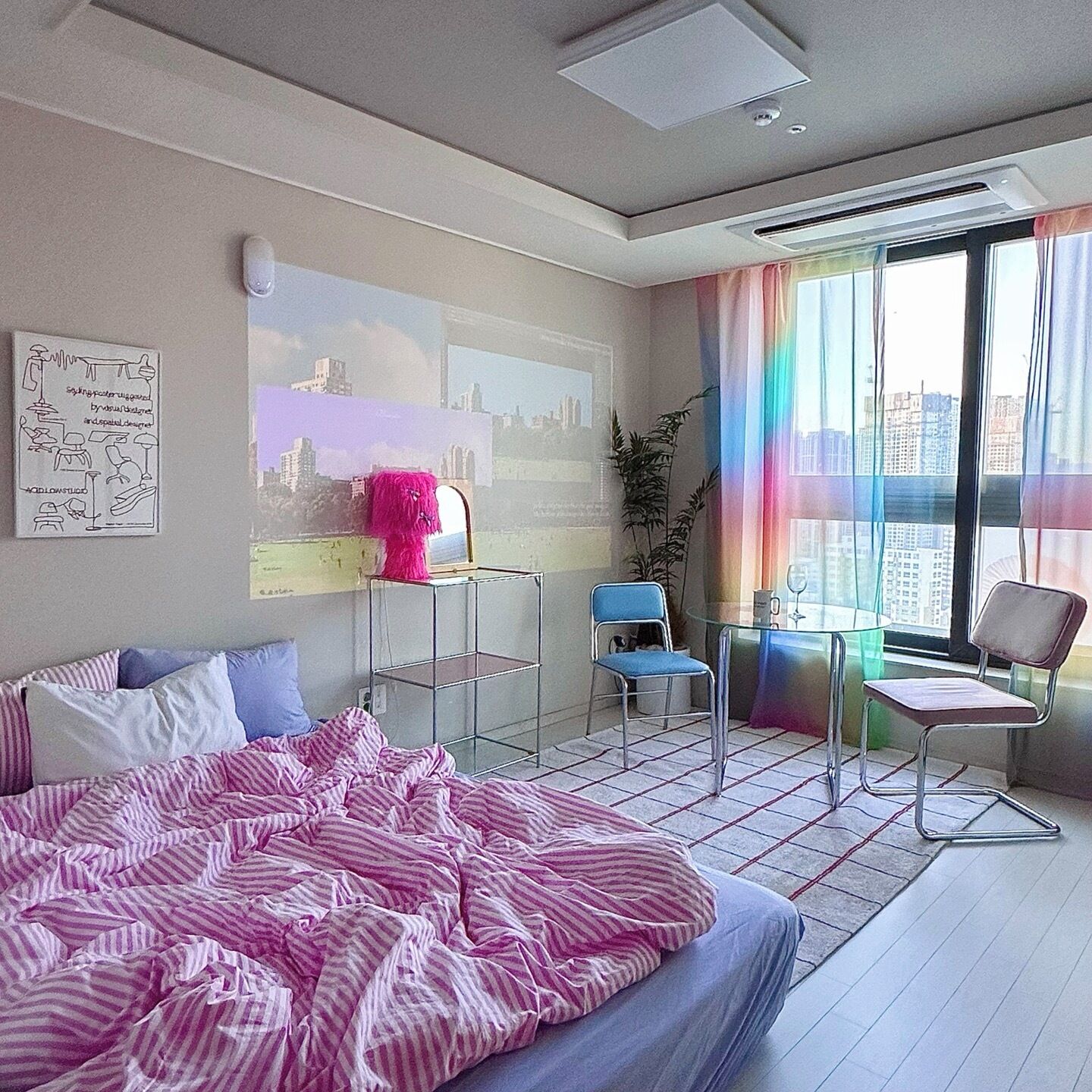 Una habitación de hotel moderna con una cama grande, un escritorio, dos sillas y vistas a la ciudad a través de amplios ventanales.