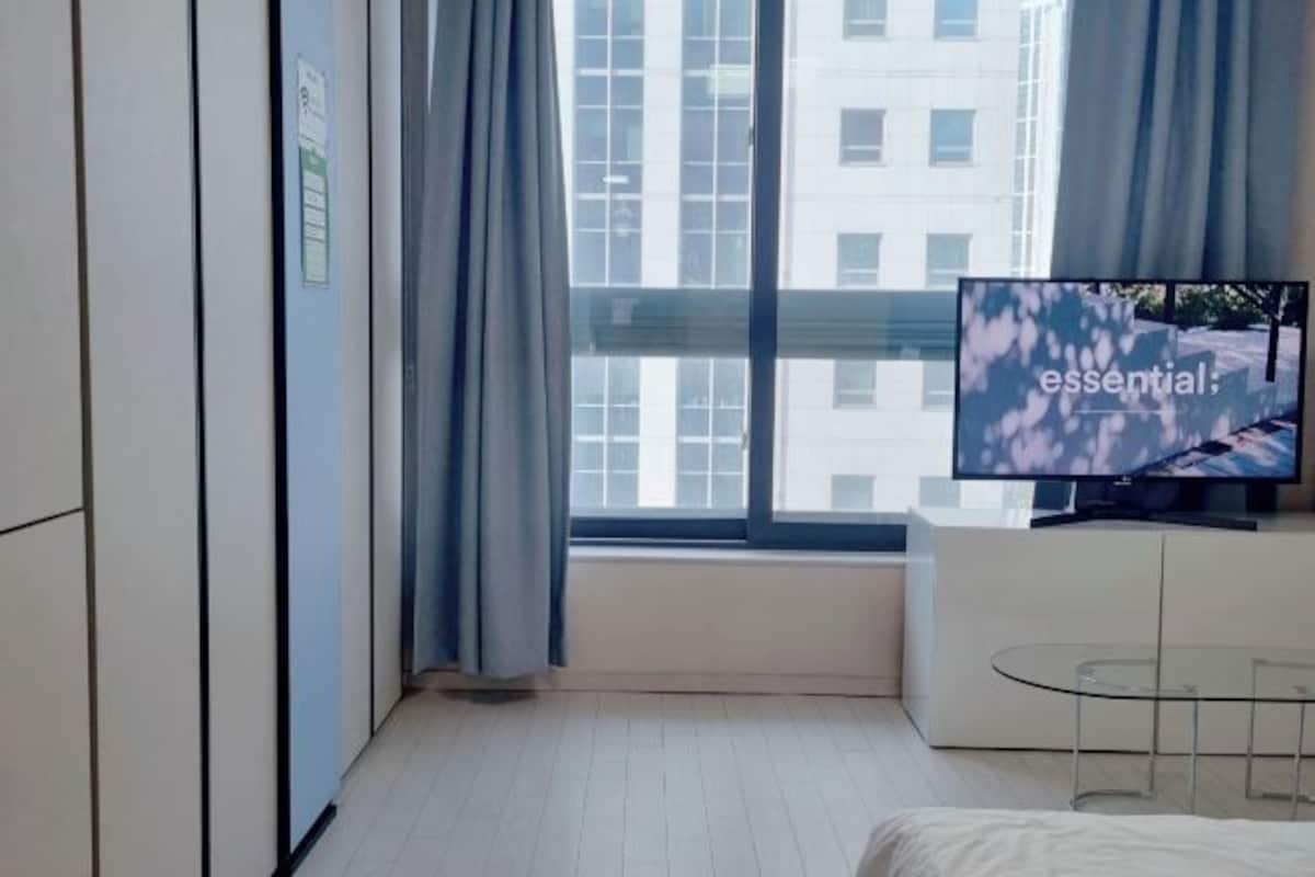 A modern hotel room with a large window, a flat-screen TV, and a glass table.