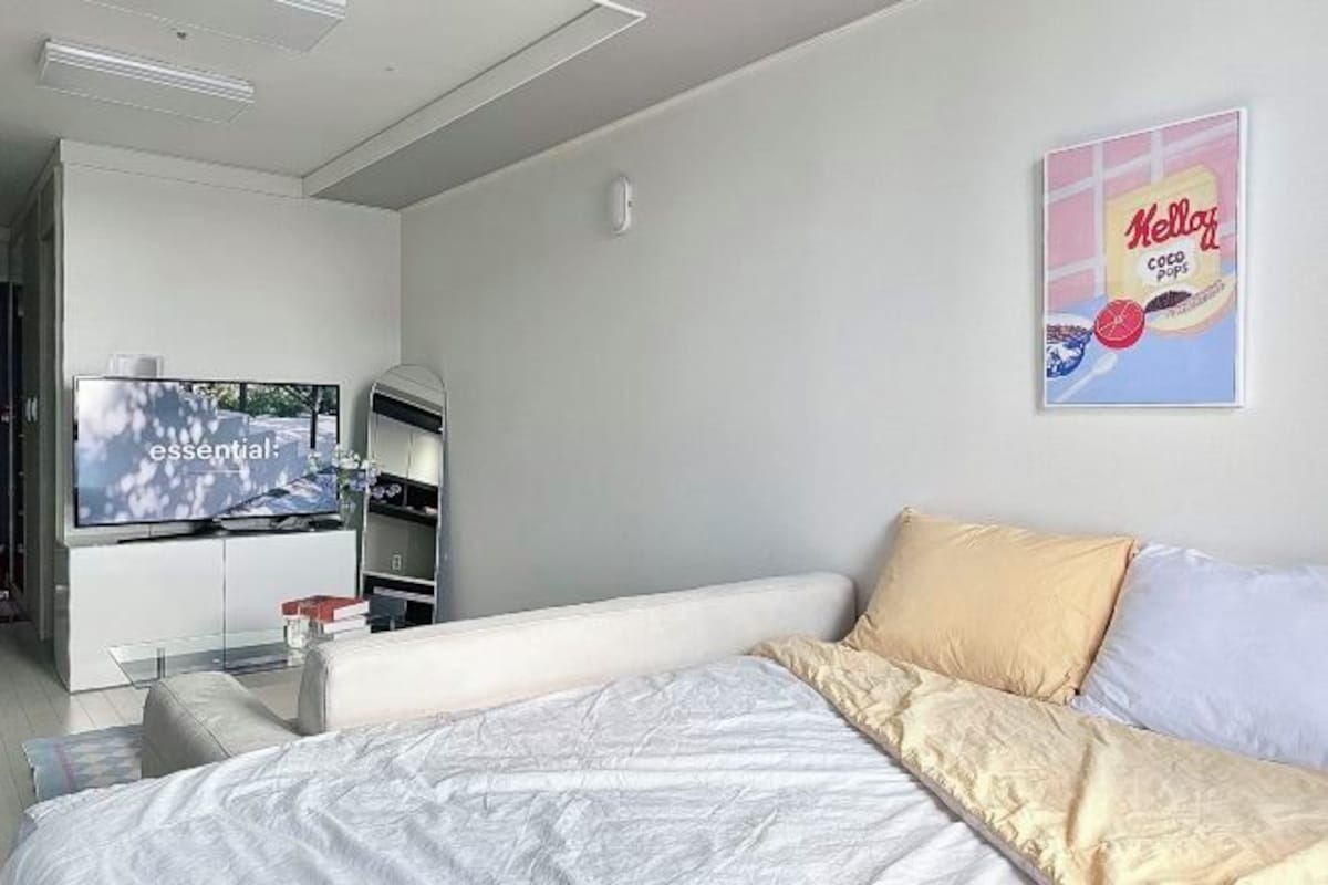 A modern hotel room with a bed, a TV, a shelf with a remote, and a poster on the wall.