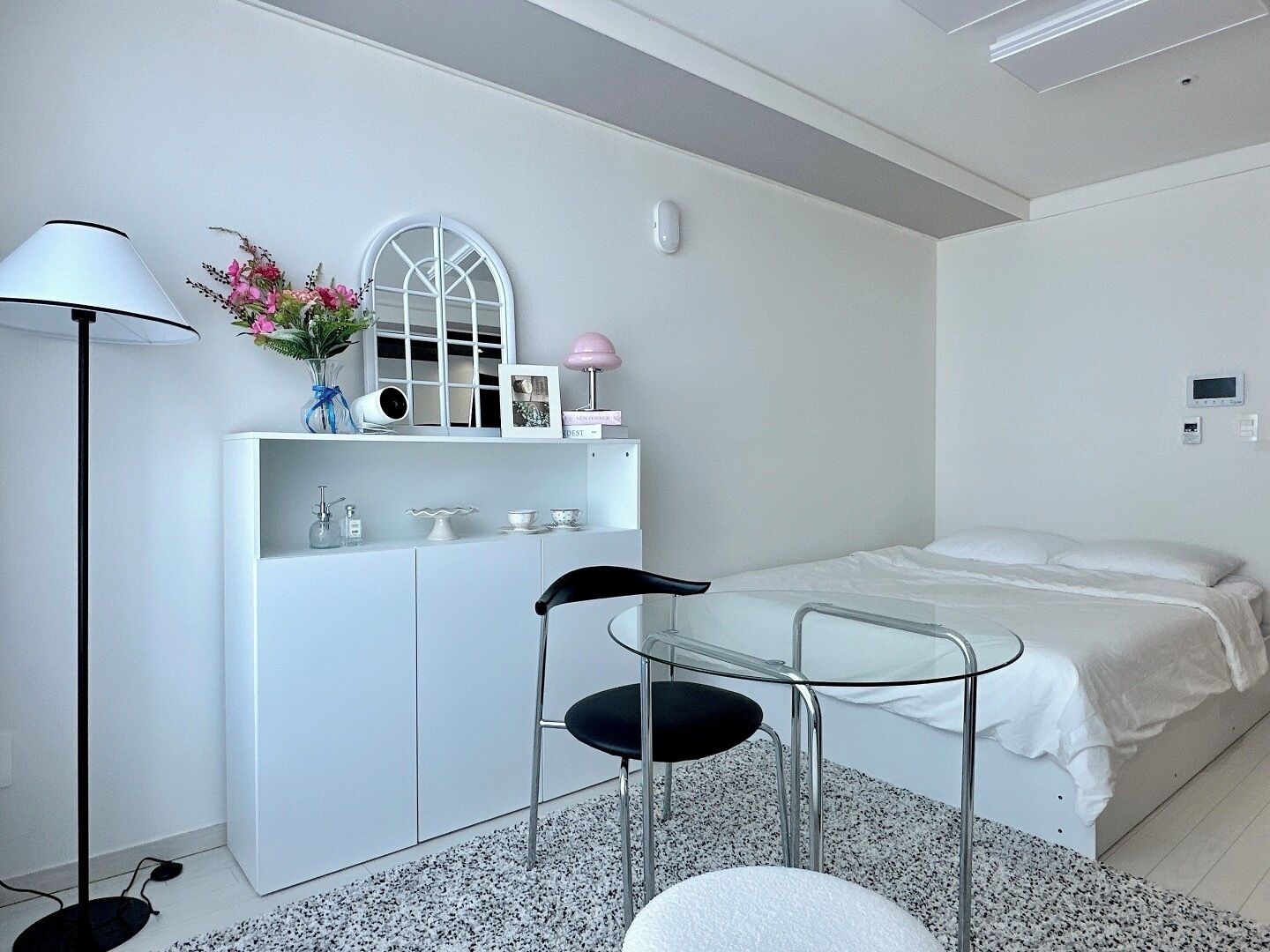 Un dormitorio moderno con una cama, un escritorio con silla, una lámpara y una mesita de noche con un florero.
