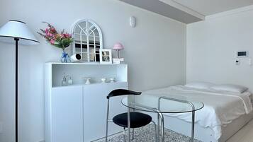 Un dormitorio moderno con una cama, un escritorio con silla, una lámpara y una mesita de noche con un florero.