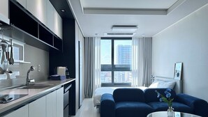 A modern hotel room with a kitchenette, a large bed, a seating area, and a view of the city.