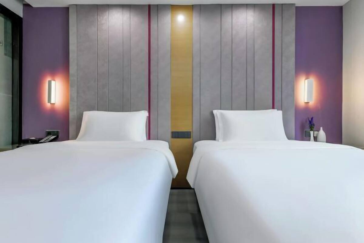 A hotel room with two beds, a central light fixture, and a wall-mounted phone.