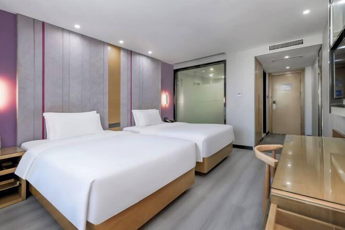 A hotel room with two beds, a wooden table, and a sliding door leading to a bathroom.