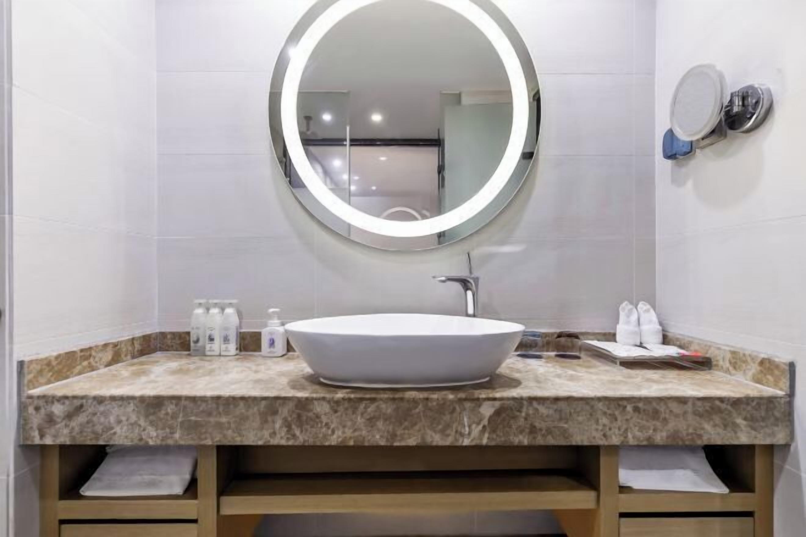 Un bagno con uno specchio tondo, un lavabo bianco e un piano di lavoro in marmo.