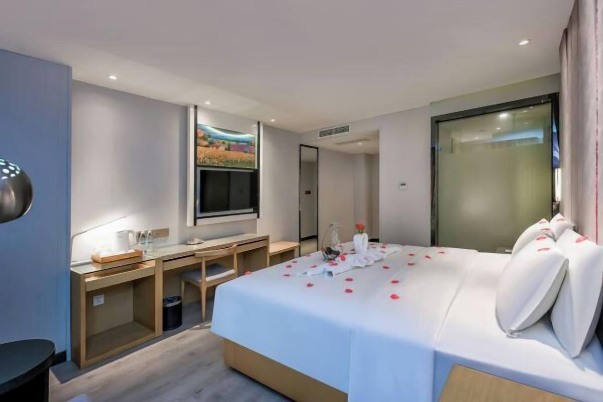A hotel room with a bed, a desk, a chair, a window, and a painting on the wall.
