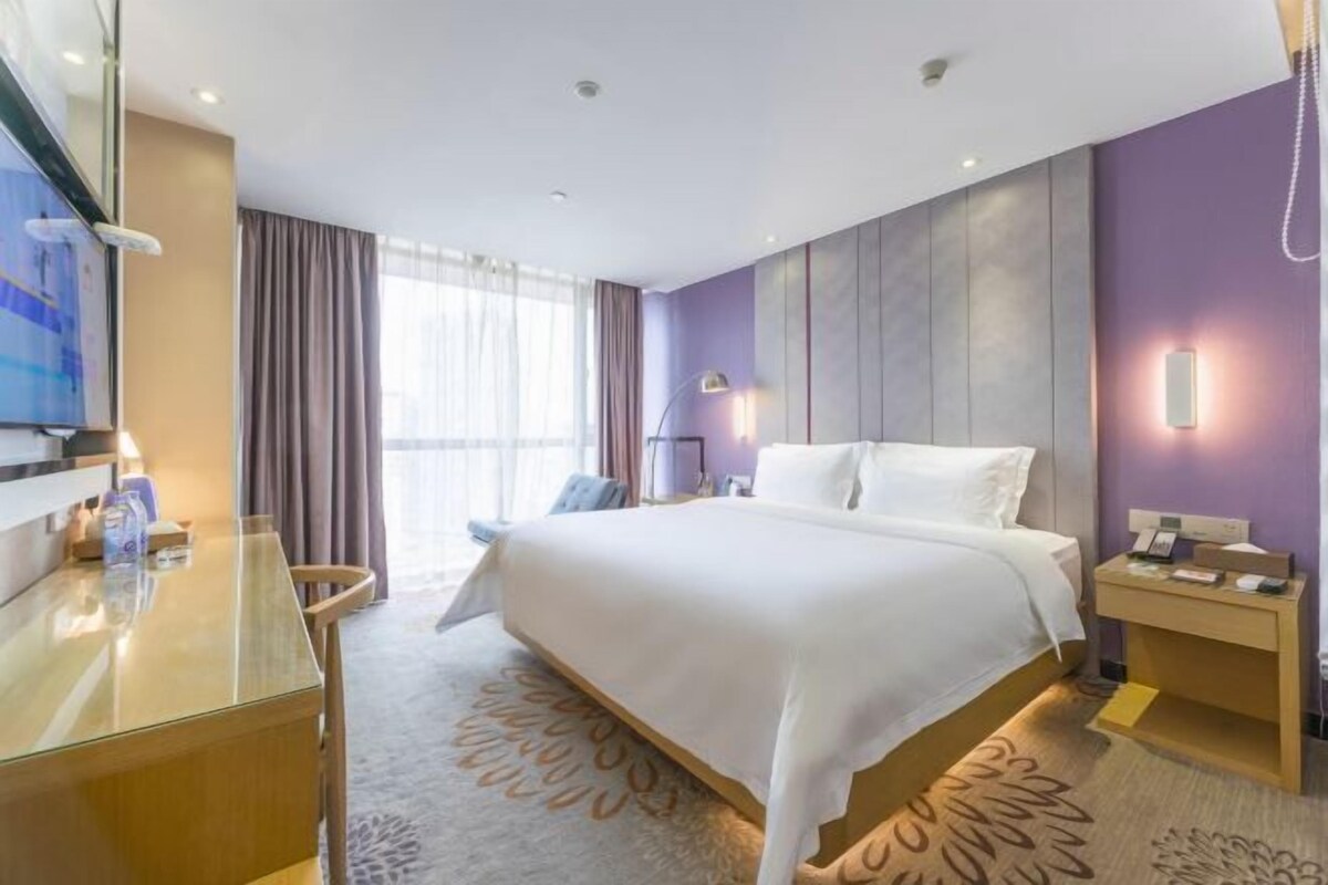 A hotel room with a bed, a desk, a chair, a TV, and a window with curtains.