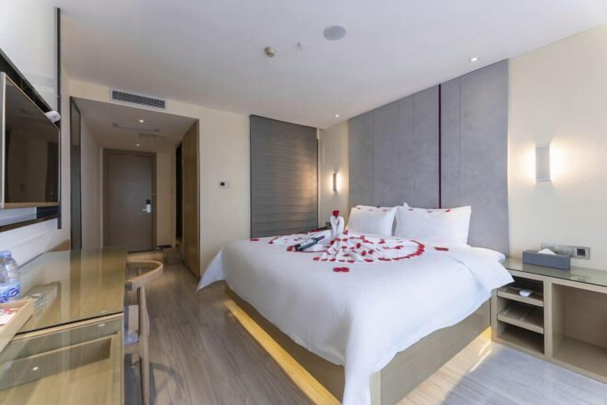 A modern hotel room with a large bed, bedside tables, a desk, and a mirror.