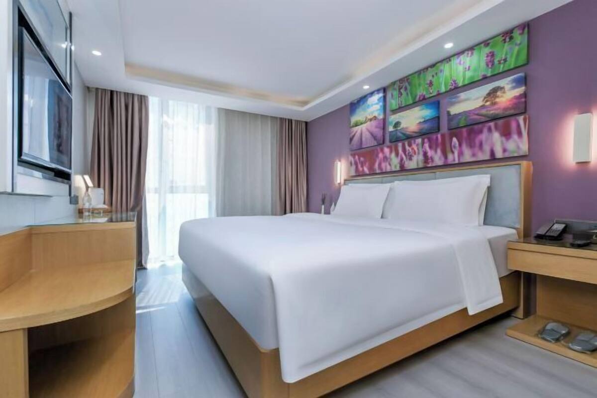 A hotel room with a bed, a desk, a TV, and artwork on the wall.