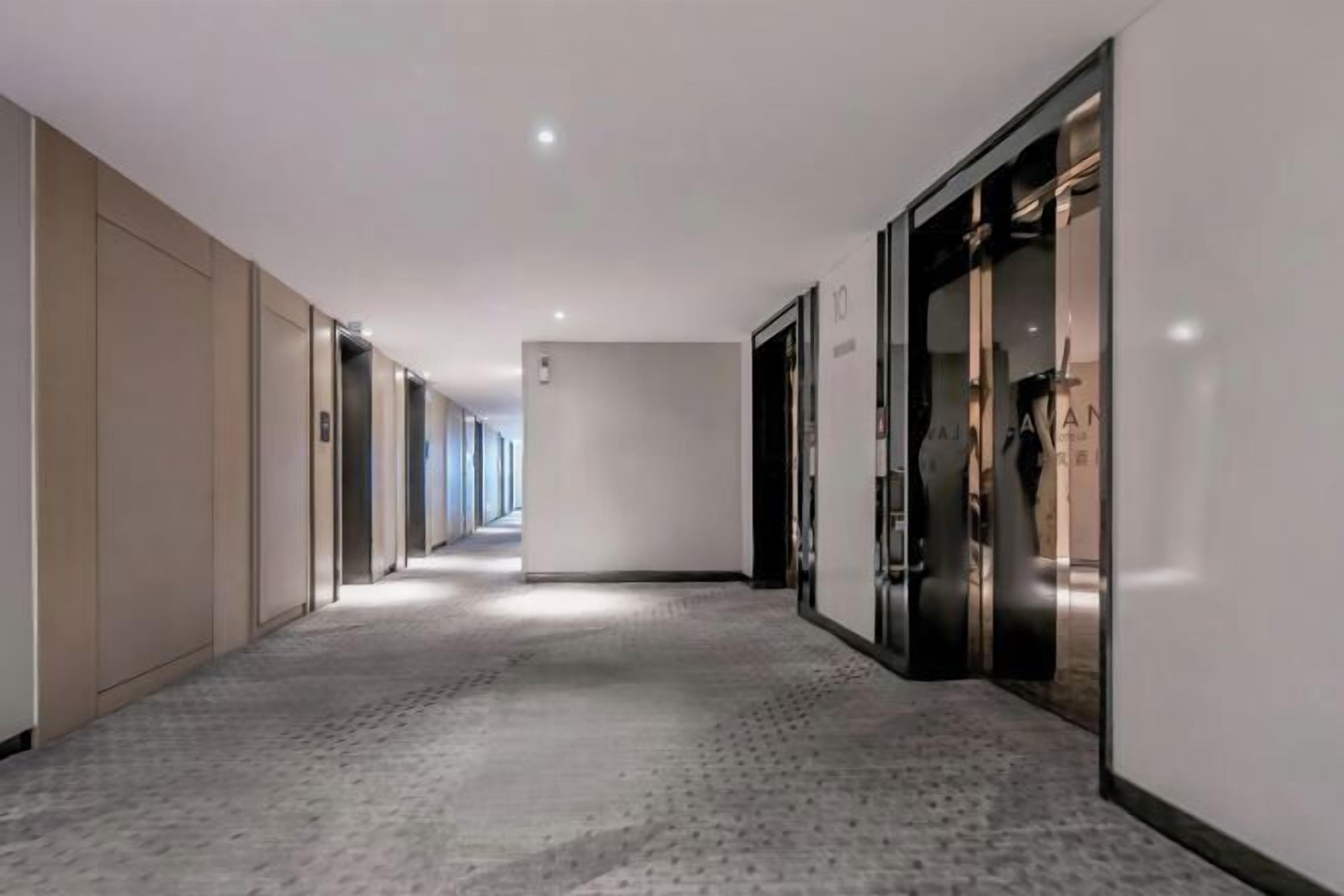 A long, narrow hallway with a patterned carpet, beige walls, and doors leading to rooms.