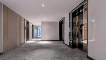 A long, narrow hallway with a patterned carpet, beige walls, and doors leading to rooms.