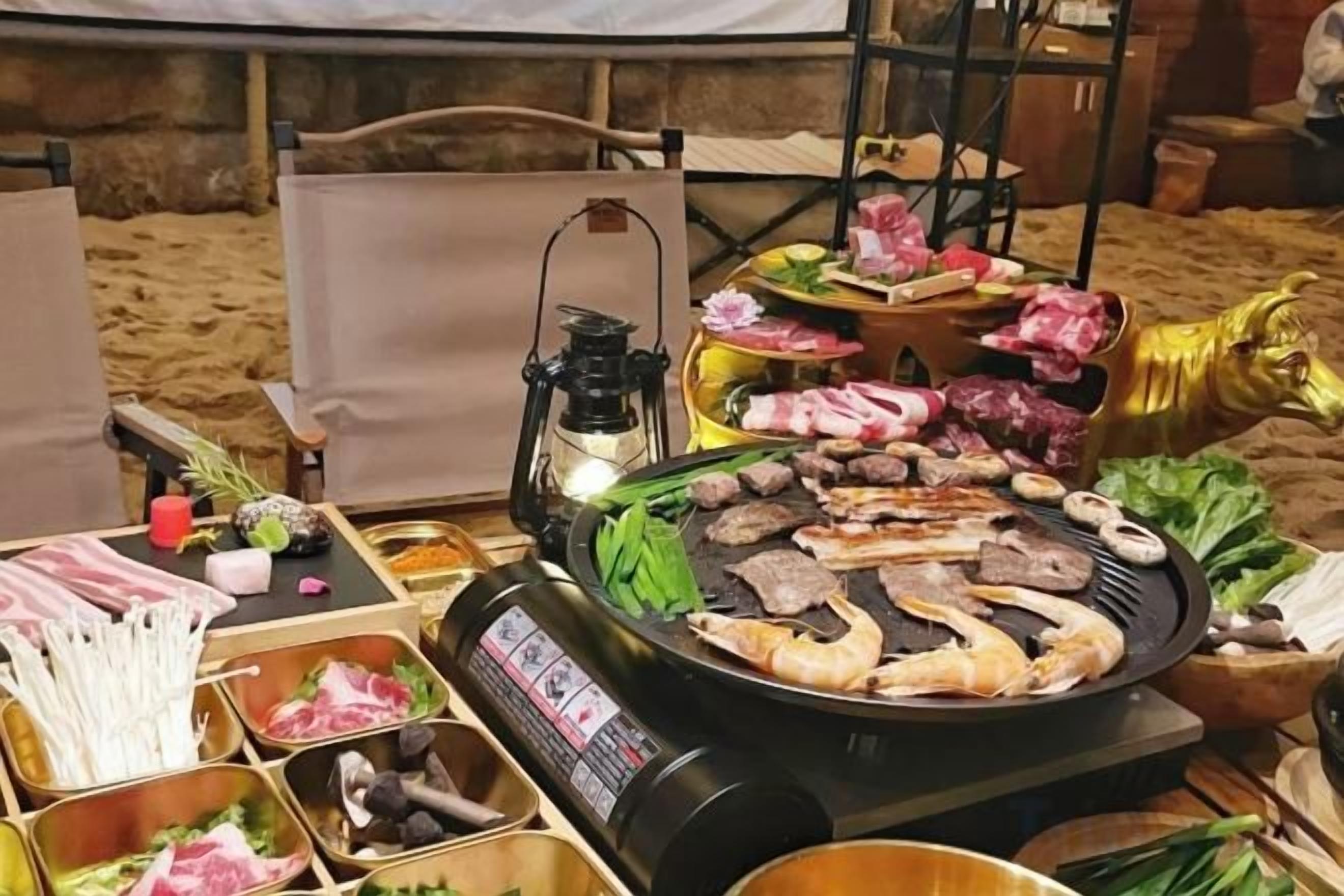 A dining setup with a grill, various meats, vegetables, and condiments.