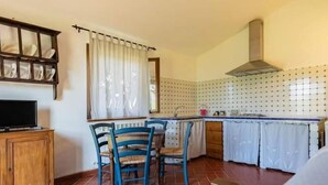 Una cuina compacta amb una façana de rajola, un armari de fusta, una televisió i una zona de menjador amb cadires.