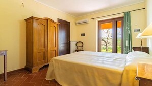 Un dormitori amb llit, armari de fusta, radiador, finestra amb vistes i una porta.