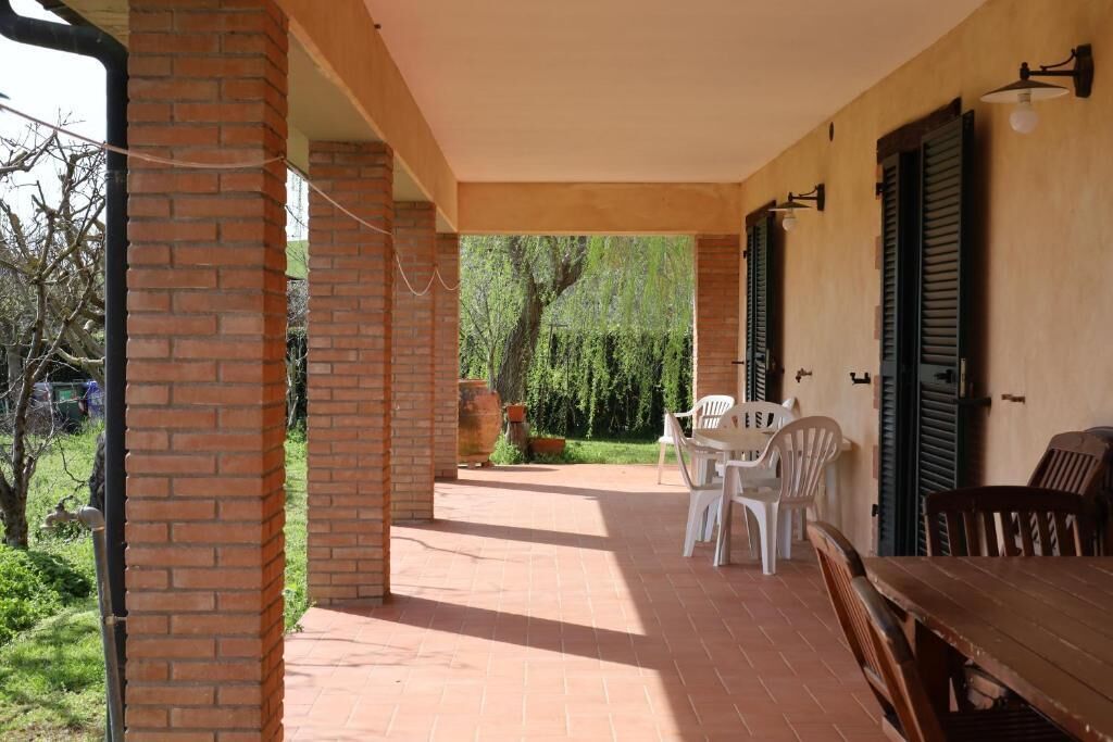 An outdoor patio with brick flooring, white plastic chairs, and a wooden table.