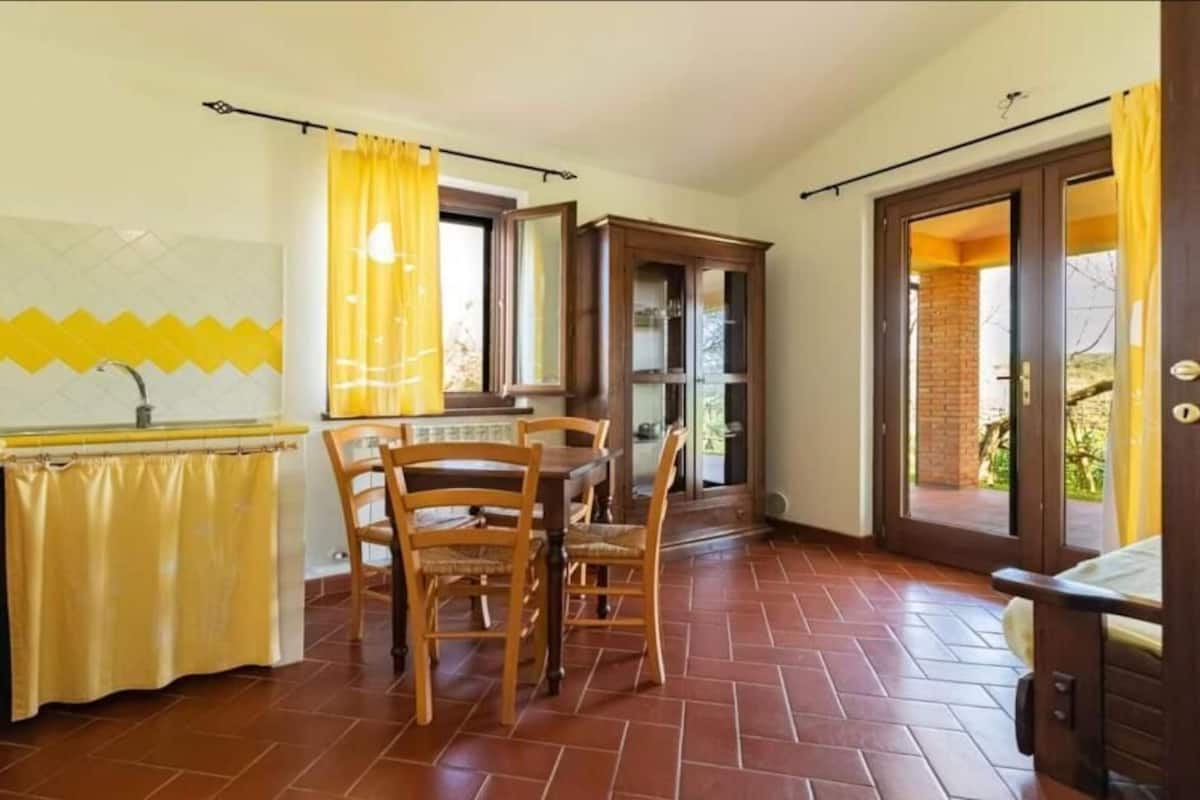 Uma cozinha compacta com área de refeições, janela com cortinas amarelas e vista para o exterior.