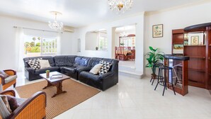 A spacious living room with a sectional sofa, a coffee table, and a bar area with stools. - Villa Paloma (Albufeira)
