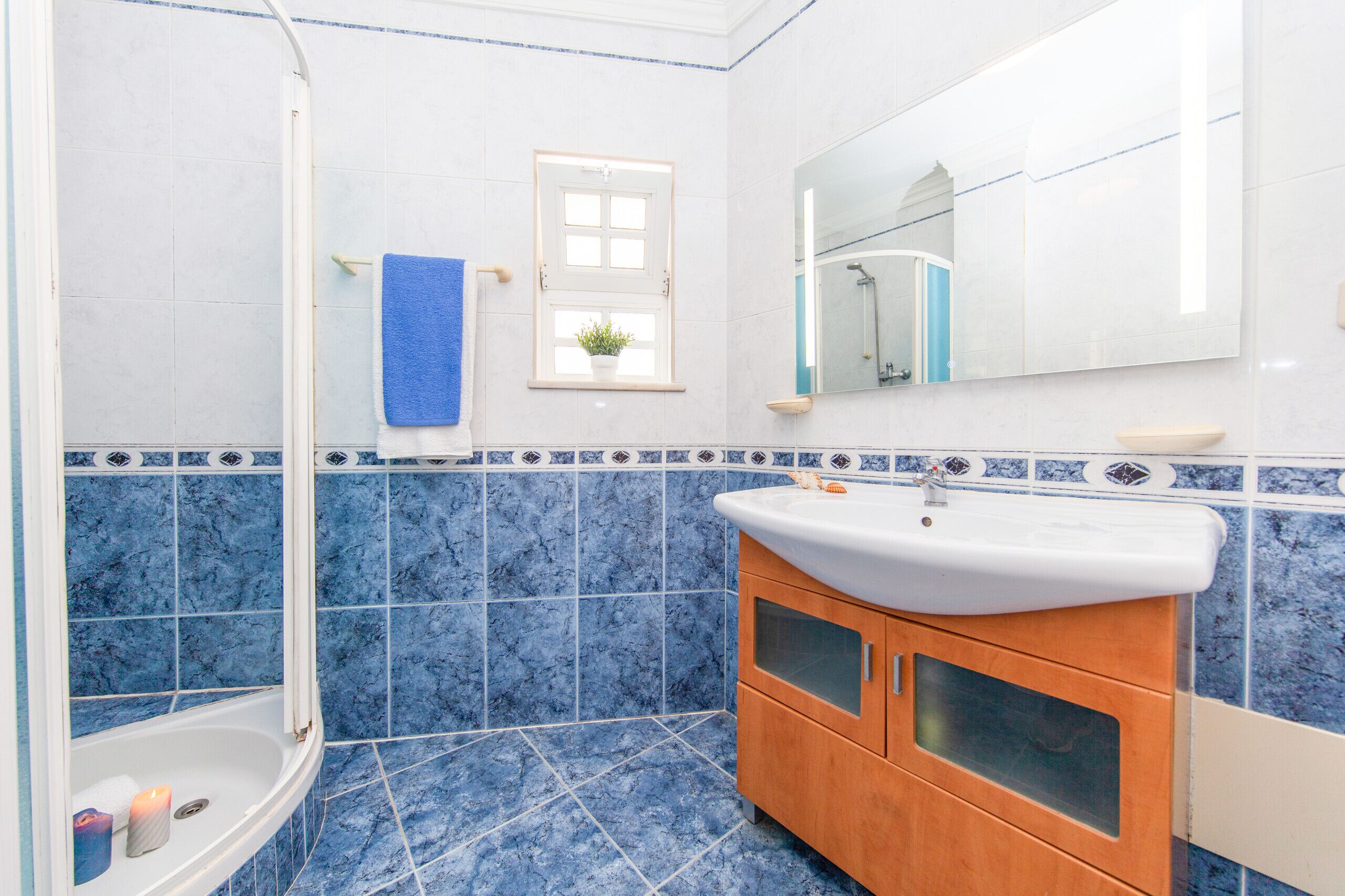 Een badkamer met een bad, een wastafel, een spiegel en een raam met een plant.