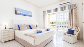 A bedroom with a large bed, a nightstand, a wicker chair, and a view of the outdoors. - Villa Paloma (Albufeira)